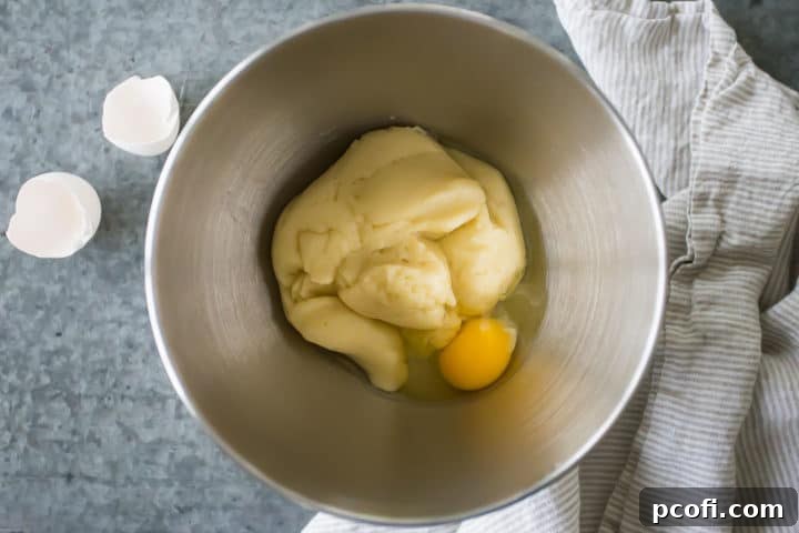 Large eggs are meticulously added one at a time into the choux pastry dough in a mixing bowl, beginning the process of enrichment for the perfect churro batter.