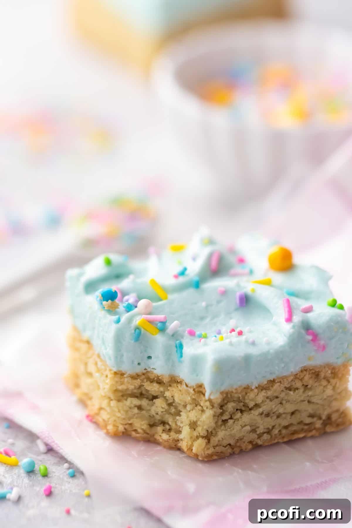 Close-up of frosted sugar cookie bars with blue frosting and rainbow sprinkles, ready to be served.