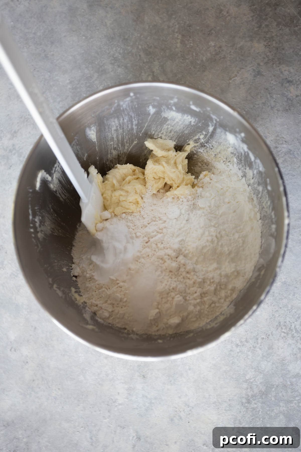 Sugar cookie dough in a mixing bowl with a spatula, showing its soft texture.