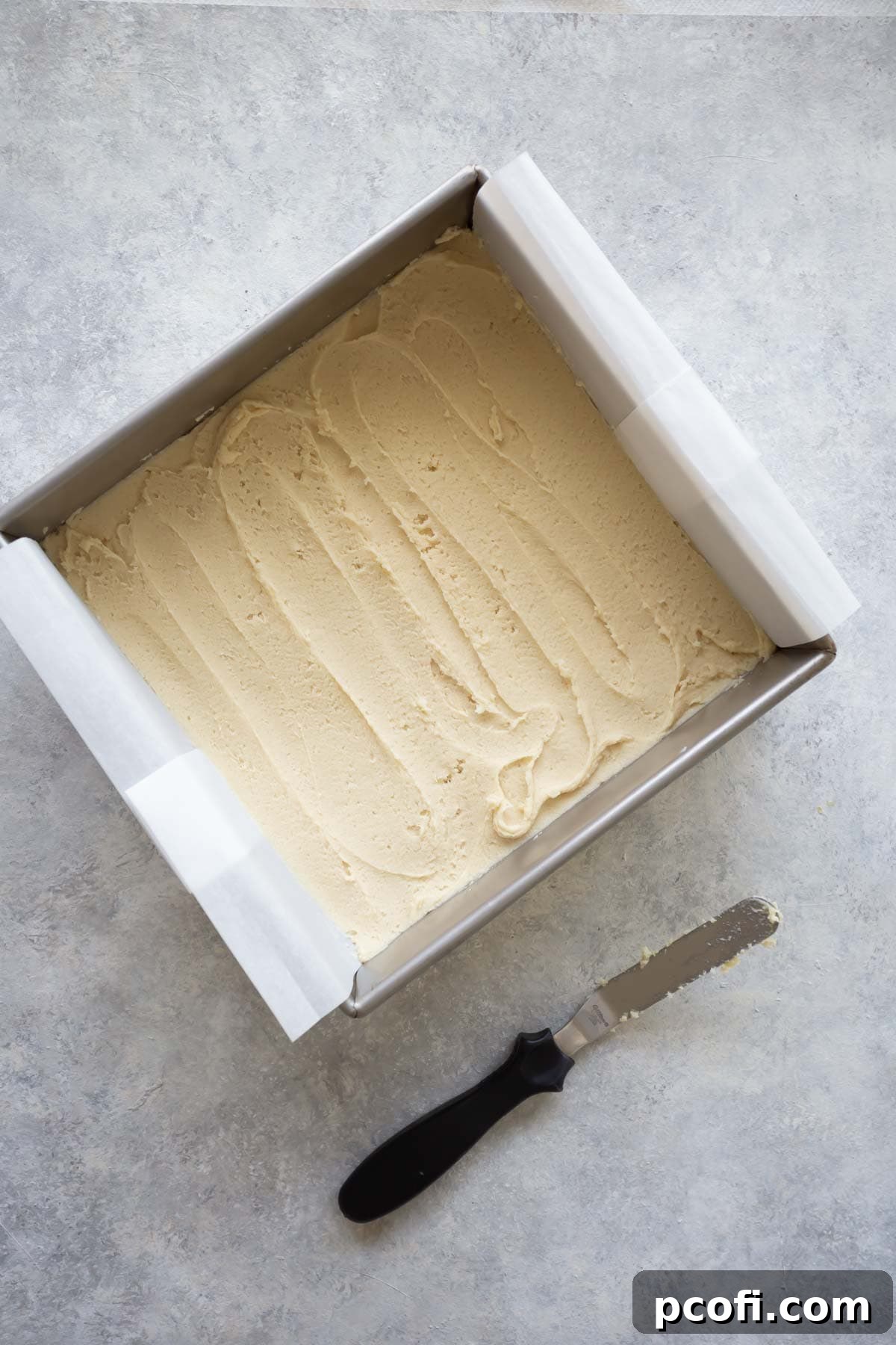 Sugar cookie dough pressed evenly into a square baking dish lined with parchment paper.