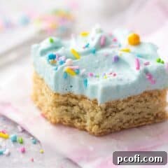 Frosted sugar cookie bars topped with frosting and rainbow sprinkles, cut into individual pieces.