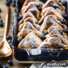Baked french toast with powdered sugar in a blue casserole dish with a copper serving spoon