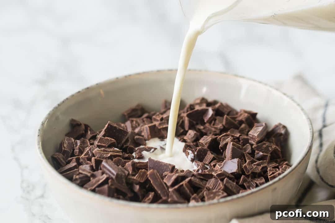 Pouring hot cream over finely chopped chocolate in a bowl, initiating the melting process.