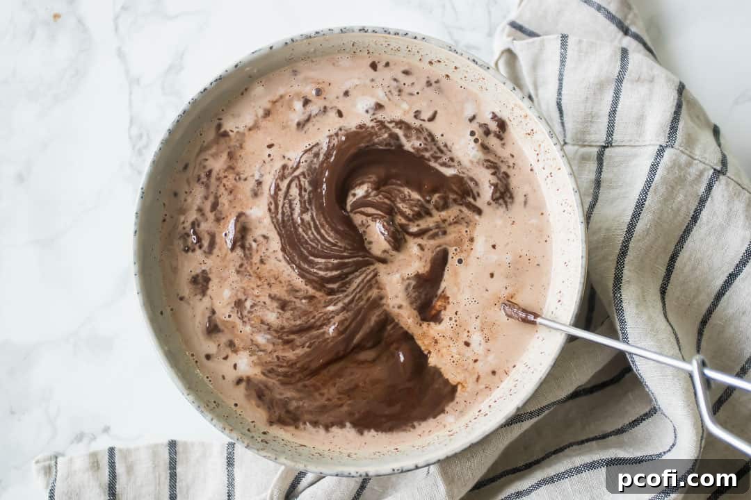 Whisking the melted cream and chocolate together until a glossy, smooth ganache forms.