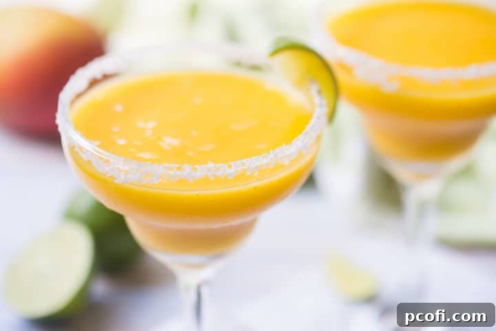 Two perfectly prepared mango margaritas in classic margarita glasses, beautifully garnished with fresh limes and mangoes in the background, signaling a perfect summer refreshment.