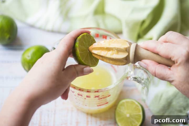 A hand juicing a fresh lime into a liquid measuring cup using a citrus reamer, emphasizing the importance of fresh ingredients for the frozen mango margarita.