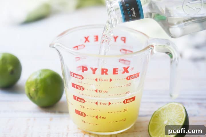 Pouring blanco tequila into a liquid measuring cup, mixing with freshly squeezed lime juice and orange liqueur for the mango margarita base.