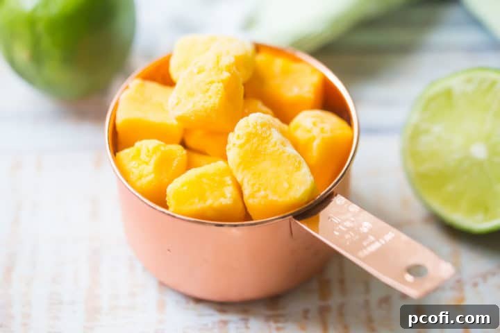 A copper measuring cup overflowing with perfectly frozen mango chunks, highlighting the key ingredient for a thick, frosty frozen mango margarita.