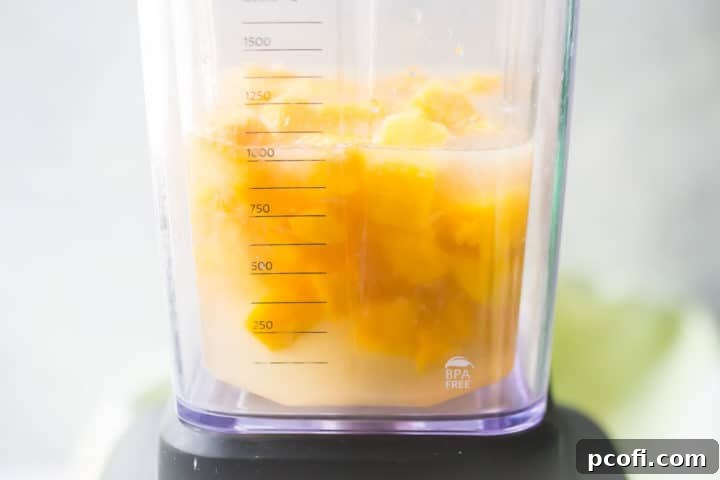 All ingredients for the frozen mango margarita, including frozen mango chunks, lime juice, tequila, and orange liqueur, being blended together in a high-speed blender to achieve a smooth, icy consistency.