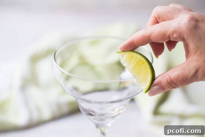 A hand wetting the rim of a margarita glass with a fresh lime wedge, preparing it for salting.