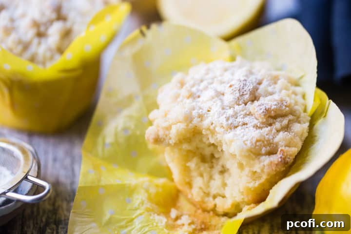 A close-up of an unwrapped lemon crumb muffin, showing its tender, moist interior and delicious streusel topping, with a bite taken out, inviting a taste.