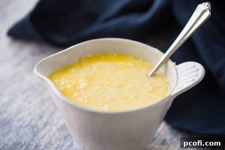 The wet ingredients for lemon muffins, a smooth mixture of melted butter, sour cream, milk, eggs, lemon juice, and lemon extract, are whisked thoroughly in a white ceramic pitcher.