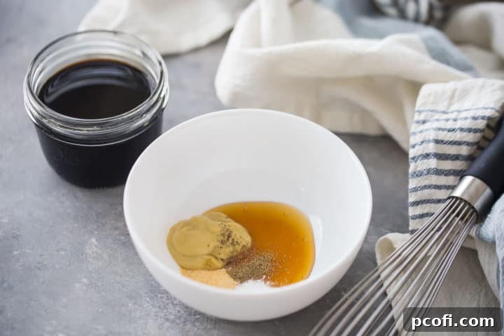 A medium bowl containing a golden mixture of honey, Dijon mustard, salt, black pepper, and garlic powder, with a bottle of dark balsamic vinegar visible in the background, showing the initial steps of preparing balsamic vinaigrette.