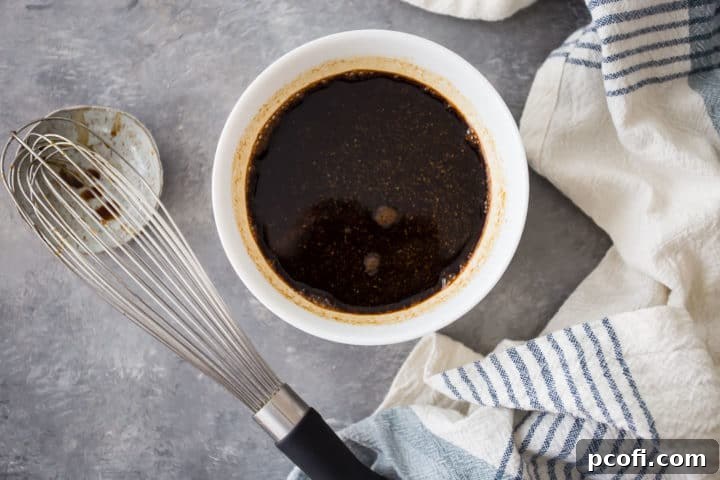 An overhead view of a bowl where balsamic vinegar has been vigorously whisked with honey, Dijon mustard, and various seasonings, creating a uniform, flavorful base for the vinaigrette.