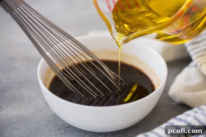A dynamic shot showing olive oil being drizzled into a bowl of whisked vinegar and seasonings, with a hand actively whisking to combine the liquids and create an emulsified vinaigrette.