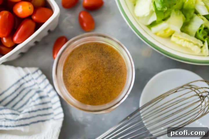 An overhead shot of a glass bowl filled with rich balsamic vinaigrette dressing, accompanied by a whisk, alongside fresh, colorful tomatoes and crisp lettuce leaves, creating an appealing culinary composition.
