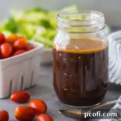 Mason jar of homemade balsamic vinaigrette dressing, with tomatoes and lettuce in the background.