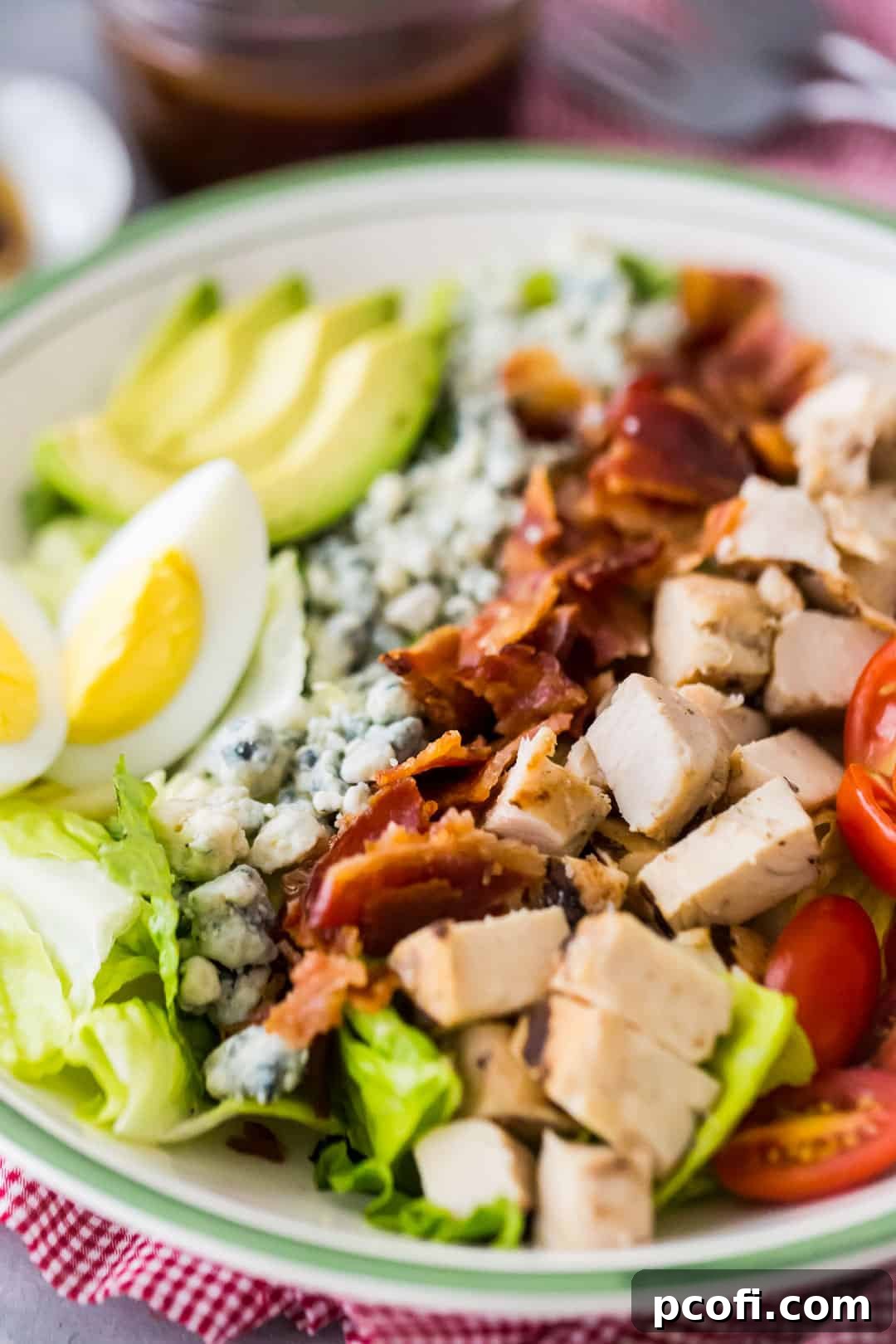 Close-up image of a large bowl of Cobb salad, with all the components arranged in neat, colorful rows over a bed of crisp greens.