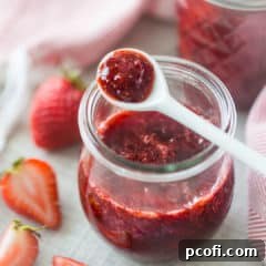 Small jar of homemade strawberry jam with a white ceramic spoon.