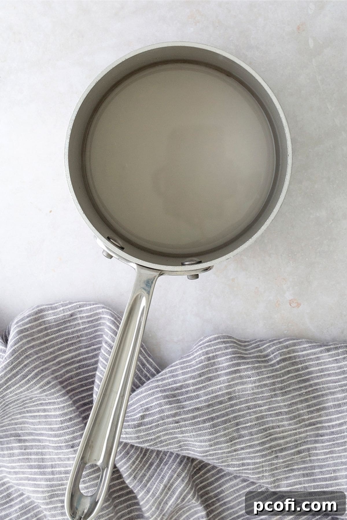 Sugar and water bubbling in a saucepan, forming a clear syrup.