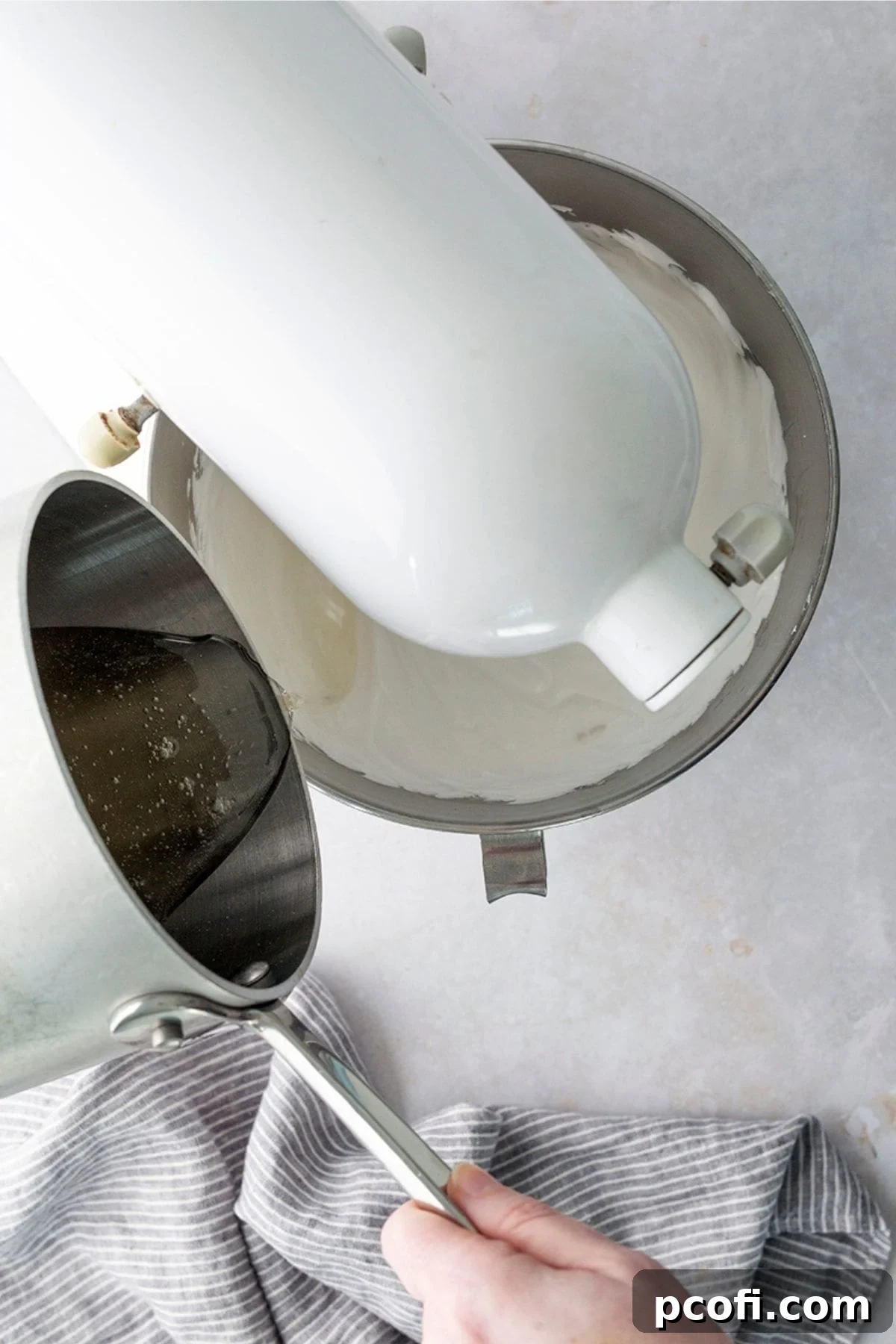 Hot sugar syrup being poured in a thin stream into whipping marshmallow frosting.