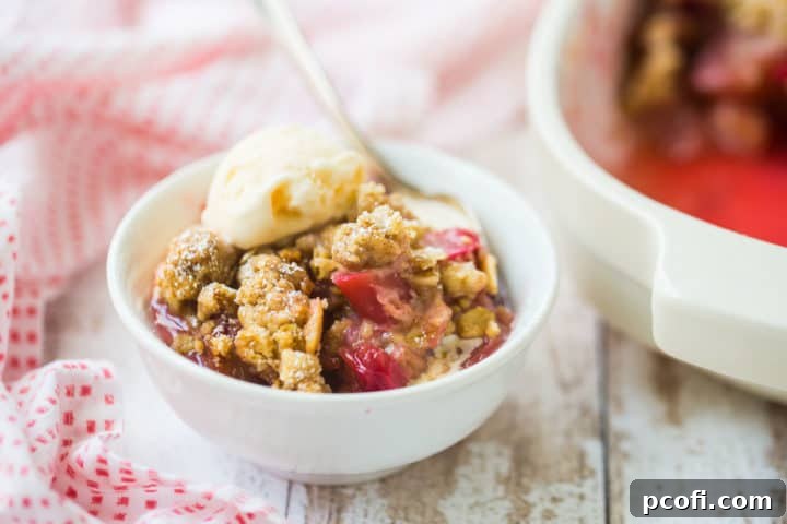 Bowl of homemade rhubarb crisp with vanilla ice cream and a baking dish in the background.