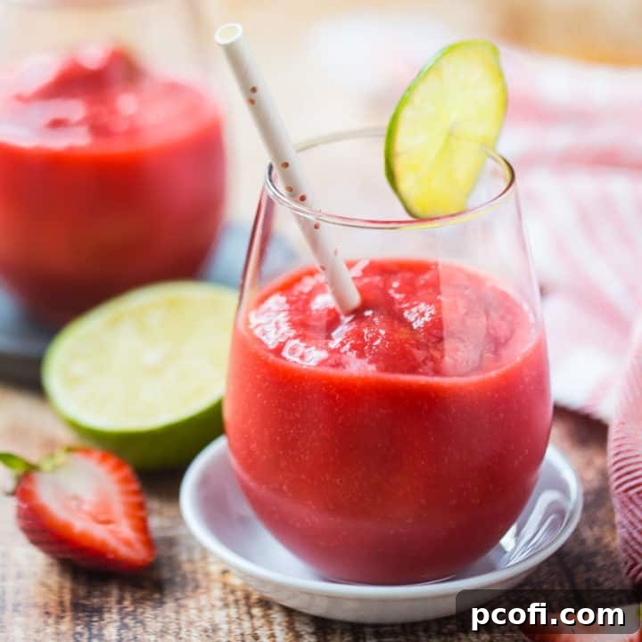 Strawberry daiquiri in a stemless wine glass with a straw and a slice of lime.