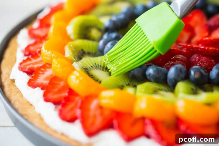 Brushing shiny glaze over fruit with a silicone pastry brush. A pastry brush gently applies a clear, glistening glaze over a colorful array of fresh fruit on a pizza.