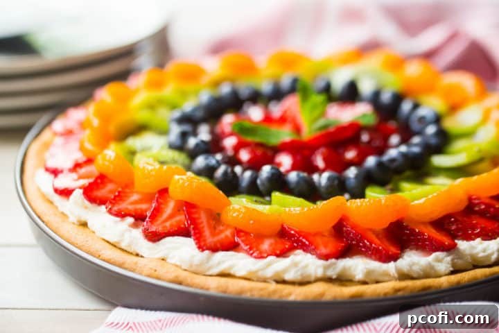 Fruit pizza made from scratch with fresh fruit, cream cheese frosting, and a sugar cookie crust. A vibrant, homemade fruit pizza on a white platter, ready to be served, showcasing its colorful fruit topping and soft cookie base.