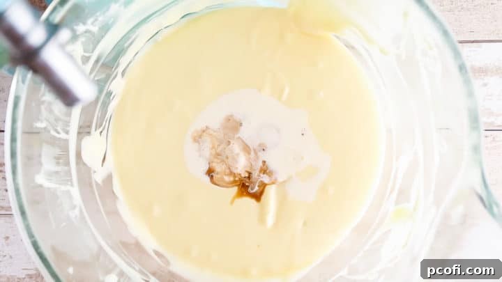Adding egg yolk, cream, and vanilla to cheesecake batter.