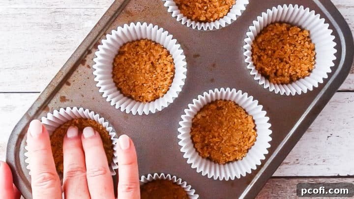 Pressing graham cracker crust into the wells of a cupcake pan.