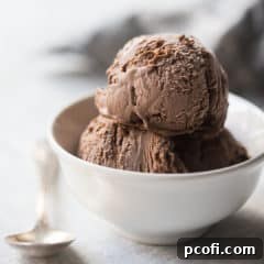 Chocolate ice cream in a small white bowl with a silver spoon, on a white background.