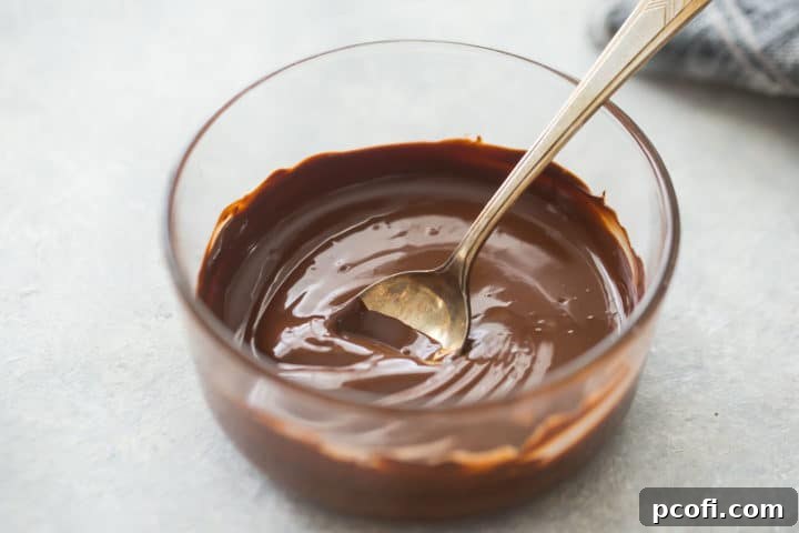 Melted chocolate in a glass bowl with a silver spoon.