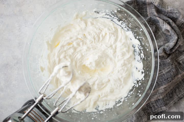 Large bowl of whipped cream with an electric hand mixer.