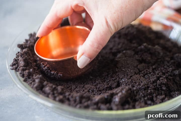 Pressing Oreo cookie crust into a pie pan with a copper measuring cup.