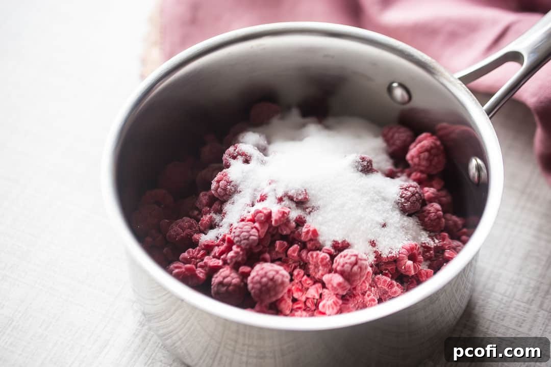Raspberries and sugar in a stainless steel pot, beginning to warm and release juices.