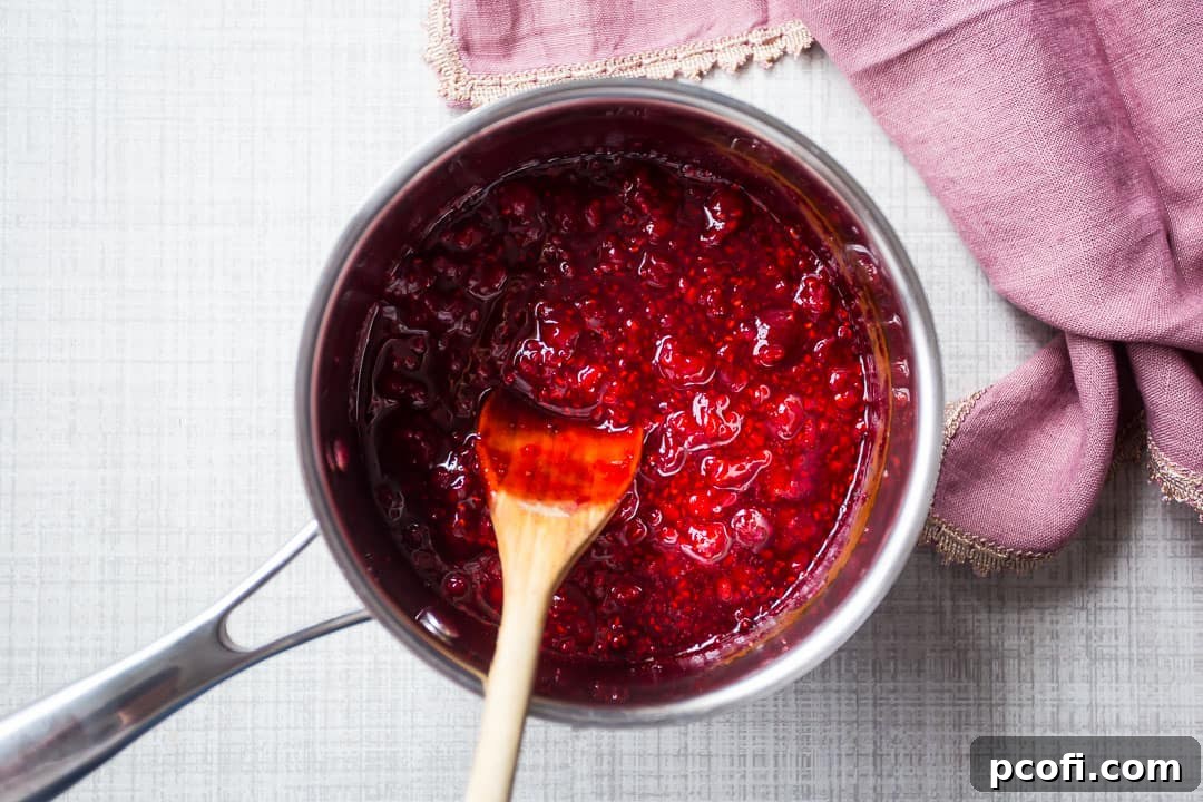 Cooked raspberries in a small pot with a wooden spoon, showing the syrupy consistency.