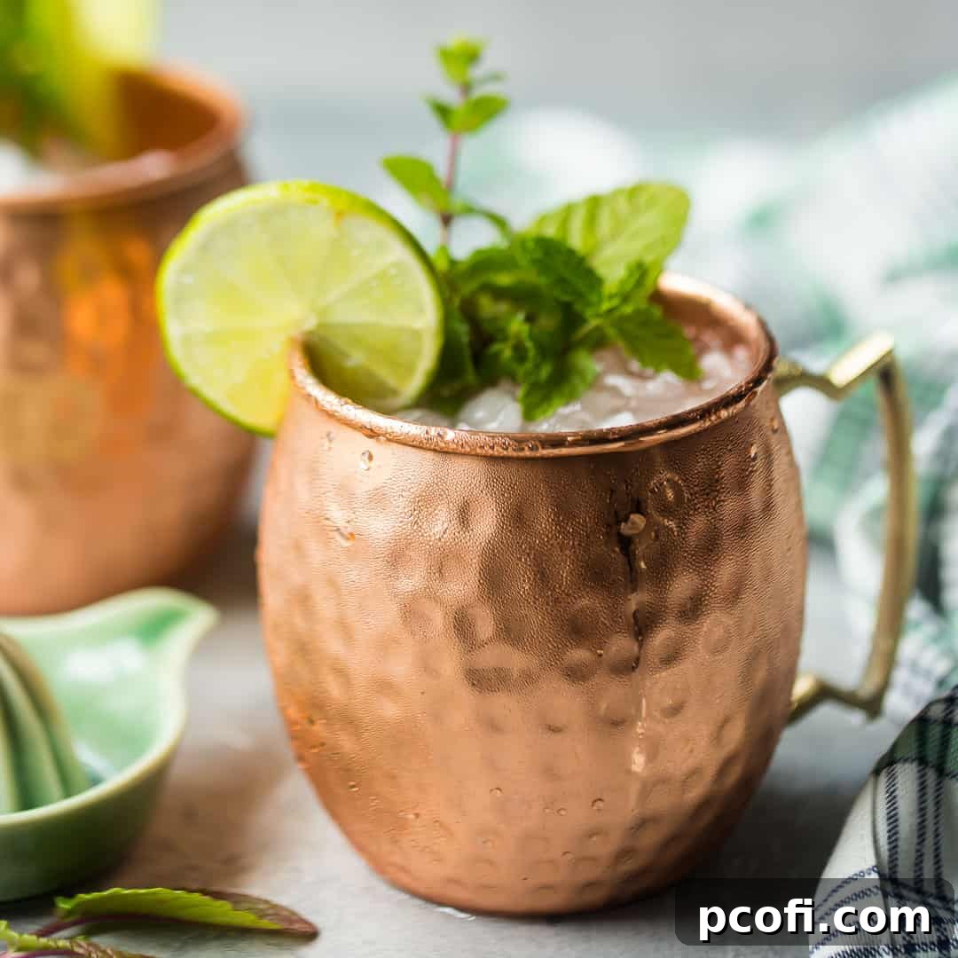 An icy Moscow Mule drink in a traditional copper mug, garnished with a fresh lime wedge and a sprig of mint.