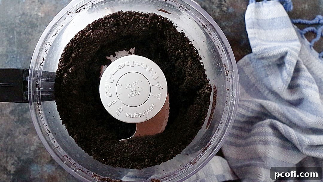 Finely ground Oreo crumbs in the bowl of a food processor, appearing like dark, damp sand, ready for butter.