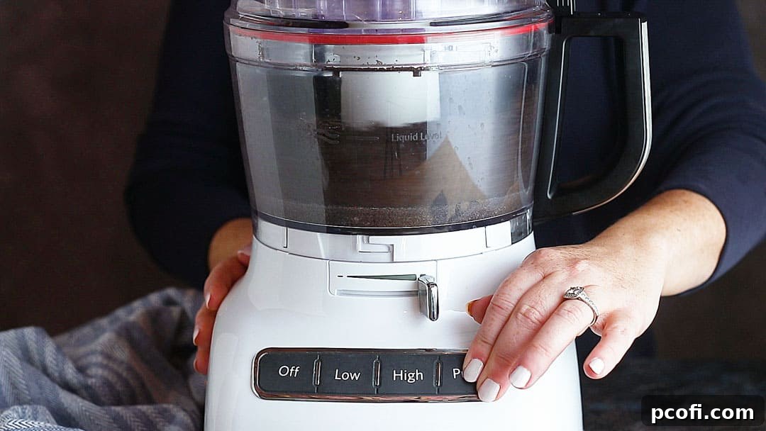 Oreo pie crust mixture being processed in a food processor, showing the crumbs and butter combining into a cohesive base.