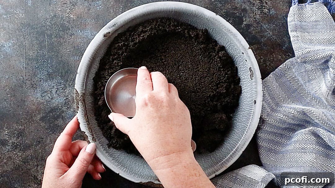 Pressing Oreo crust into a pie dish with the flat bottom of a measuring cup, creating an even, smooth layer.