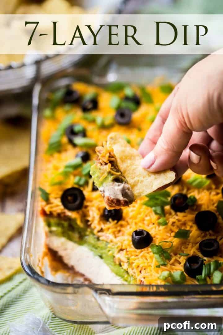 A tortilla chip scooping a generous portion of creamy 7-Layer Dip, highlighting the distinct layers of the popular appetizer.