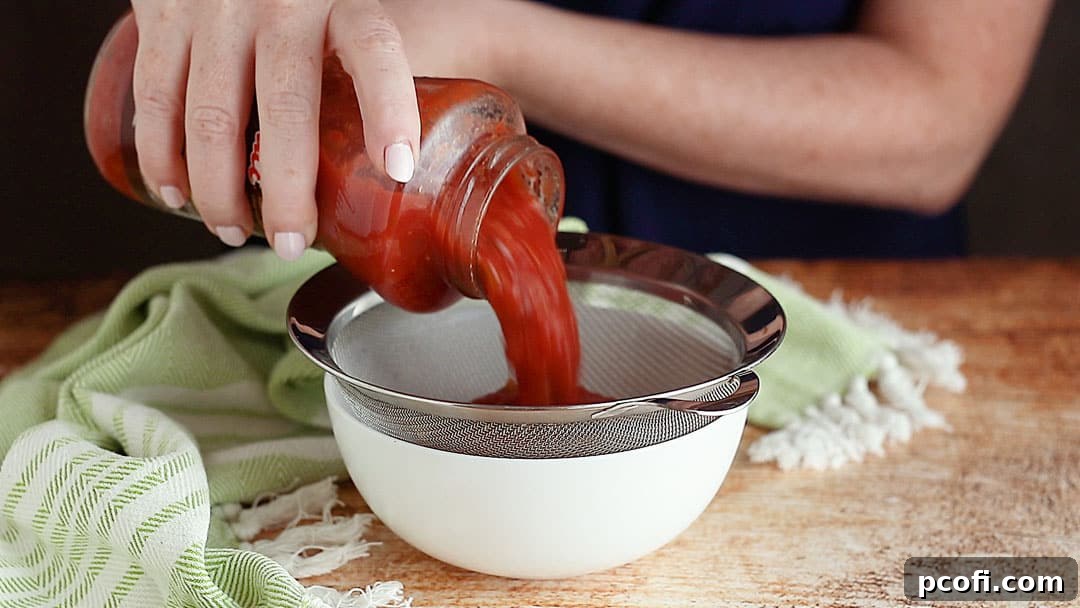Pouring fresh salsa into a fine mesh strainer to remove excess liquid for a firmer dip texture.