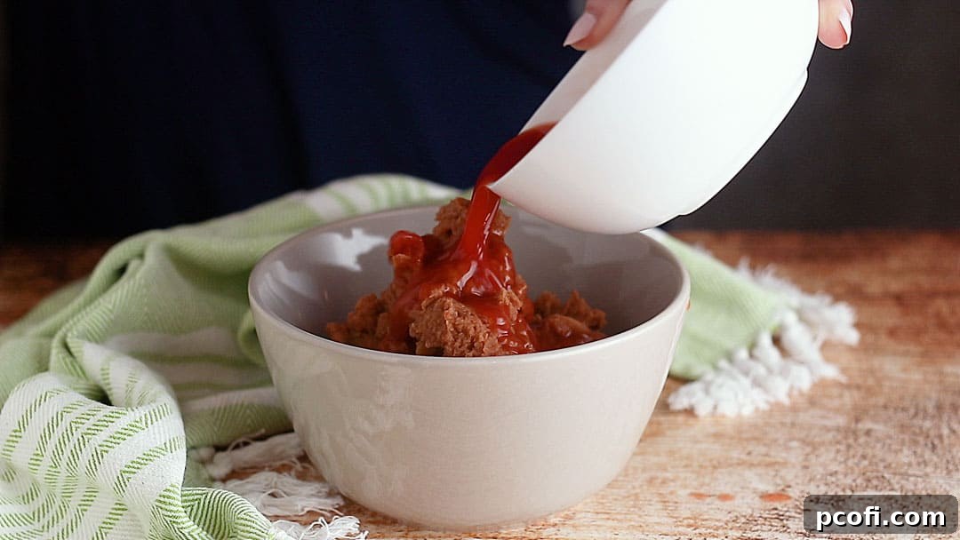 Adding reserved salsa liquid to refried beans in a bowl to achieve a smoother, more spreadable consistency for the dip's base layer.