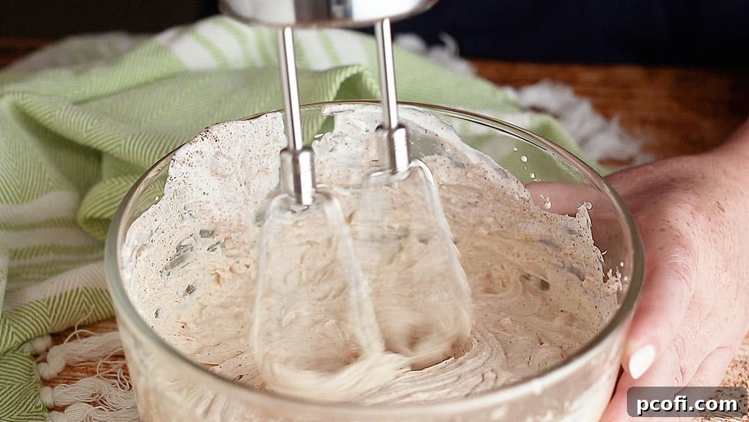 Mixing cream cheese, sour cream, and spices with an electric mixer to create a smooth, seasoned creamy layer for the 7-Layer Dip.