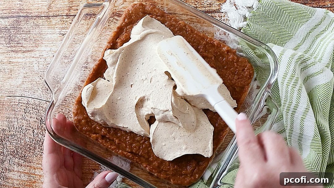 Spreading the seasoned cream cheese and sour cream mixture evenly over the refried bean base in a glass dish.