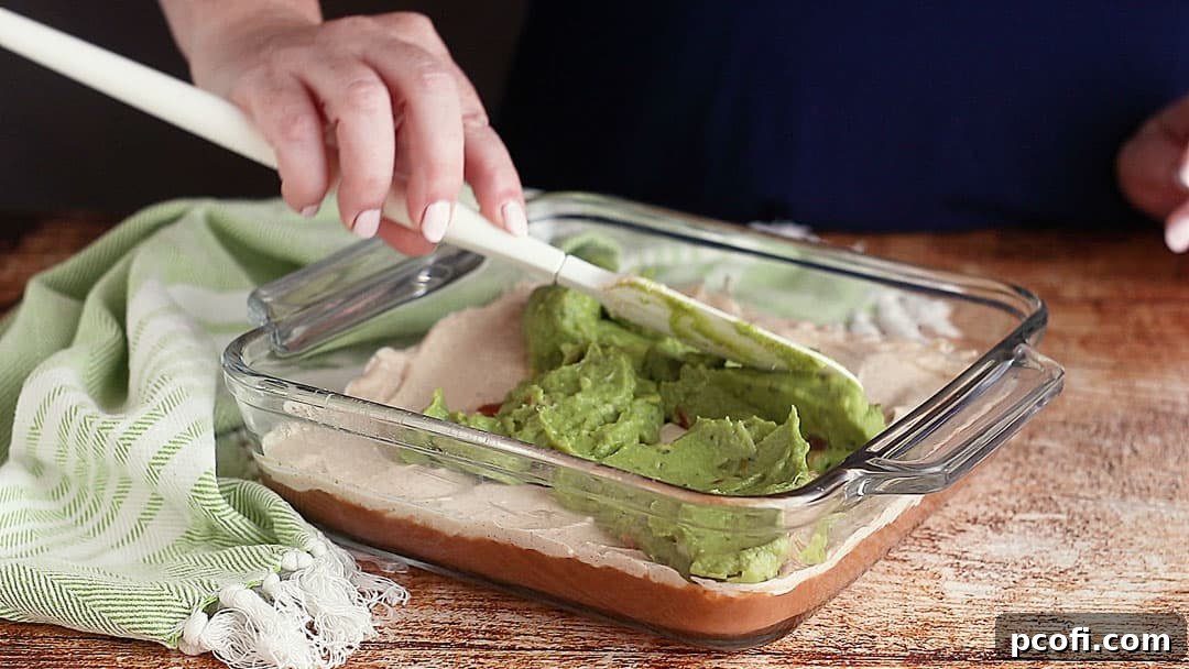 Carefully spreading a layer of fresh guacamole over the seasoned cream cheese mixture in the 7-Layer Dip.