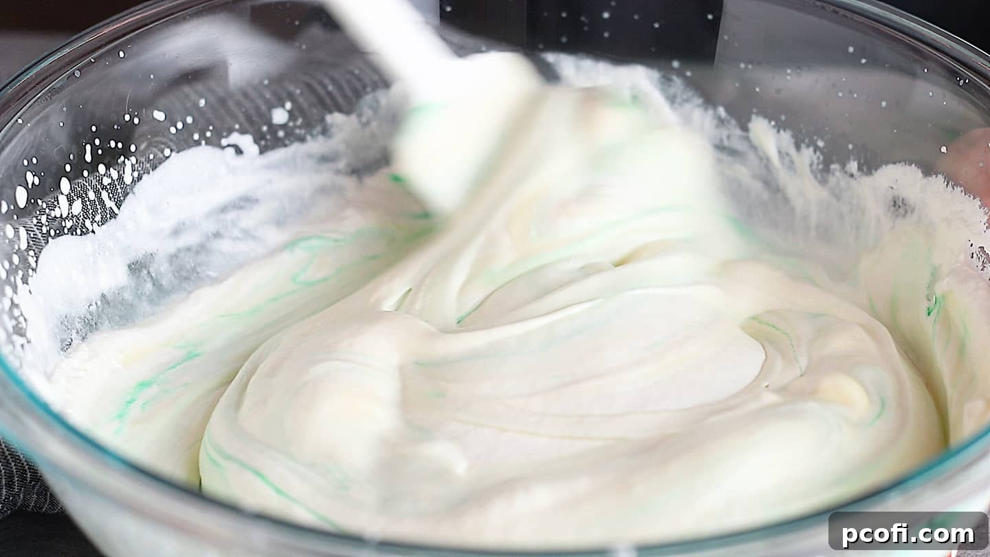 Folding the vibrant green mint chocolate chip ice cream base, showing the smooth, creamy texture.