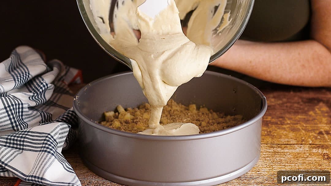 The final layer of cake batter is carefully spread over the apples and cinnamon streusel, ready to bake and puff up in the oven.