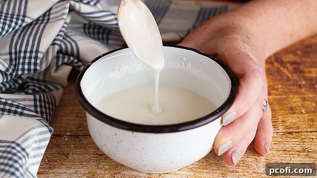 A small enamel bowl holds a luscious powdered sugar glaze, with a spoon dripping the sweet liquid, illustrating its perfect drizzling consistency.